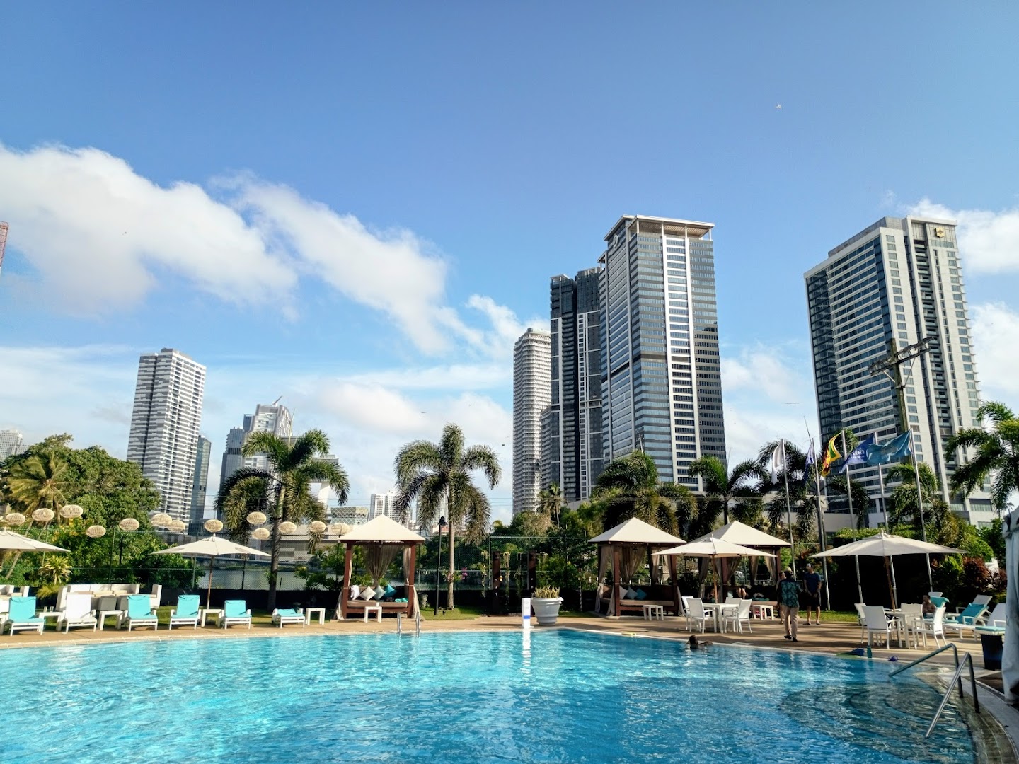SunsetBlu daytime pool with palm trees and Colombo city skyline, sun loungers and parasols