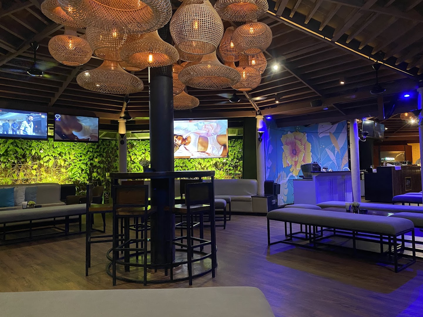 SunsetBlu interior lounge with rattan pendant lights, floral mural, and ambient blue lighting